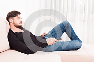 Male laying on sofa holding remote control