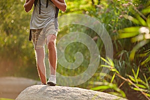 Male legs hiking at mountain peak. Trekking shoes on hiker feet outdoors crossing rock stones on river creek.