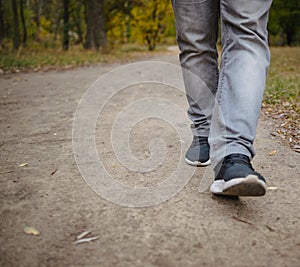 Male legs in jeans and sneakers walking out into the distance on the ground covered with fallen yellow leaves. Autumn arrival