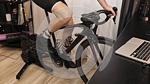 Male legs are spinning pedals on exercise bicycle at home. Professional cyclist is cycling on indoor cycling trainer. Indoor cycli