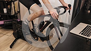 Male legs are spinning pedals on stationary bicycle. Cyclist is cycling on indoor smart bike trainer at home. Indoor cycling. Fitn