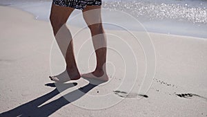 Male legs walking along sea coastline. Man spending summer holiday at seaside leaving footprints at wet sand beach