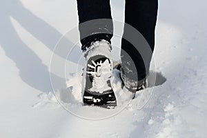 Male legs in winter shoes walking on snow covered path. Close -up