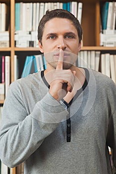 Male librarian making a sign to be quiet in library