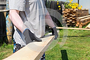 A male loader carries a wooden Board. Yard with a warehouse of lumber.