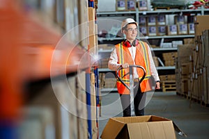 Male logist in the warehouse stands with a pallet loader and unloading goods.