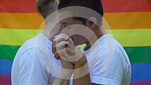 Male lovers enjoying closeness, holding hands lgbt flag background, acceptance