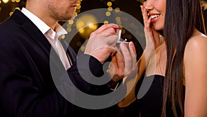 Male making proposal to girlfriend at party, presenting diamond ring, engagement