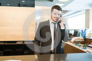Male Manager Confirming Order For Booking Accommodation On Phone In Hotel