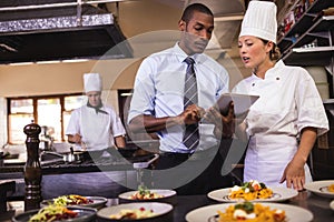 Male manager and female chef using digital tablet in kitchen