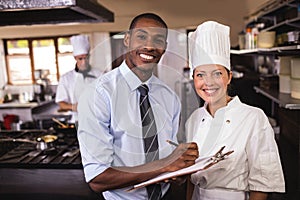 Male manager and female chef writing on clipboard in kitchen