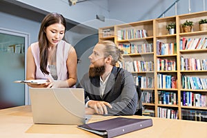 Male manager and female secretary consult work. Female employee pointing finger laptop presenting information with paper document