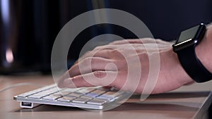 Male manager typing on the keyboard in the office in the evening. A smart watch is worn on the hand. Close-up.