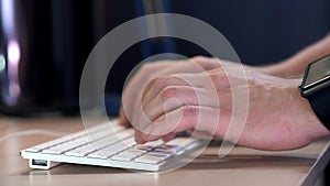 Male manager typing on the keyboard in the office in the evening. A smart watch is worn on the hand. Close-up.