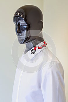 Male mannequin dressed in a white shirt with embroidery on the collar on a light beige background.