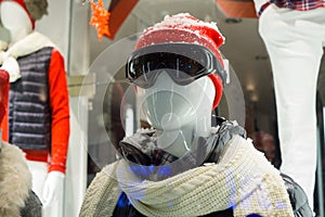 Male mannequin in store window during winter with ski gear, woolly hat, dark goggles, scarf, down jacket and fake snow on head