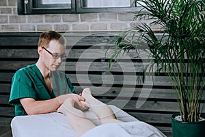 A male massage therapist massages the feet and legs of legs.