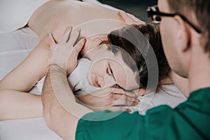 The male masseur is doing massage shoulder of a young woman. Beautiful relaxed face of a young woman with brown hair