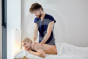 male masseur massaging back and shoulder blades of female lying on massage couch at spa