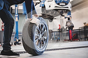 Male mechanic hold and rolling tire at repairing service garage background. Technician man replacing winter and summer tyre for