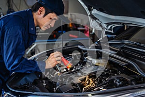 Male mechanic holding and shining flashlight to checking car engine problem