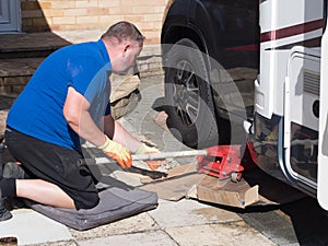 A male mechanic kneels down on a kneeling mat using a trolley jack ready to lift a motorhome front wheel. RV