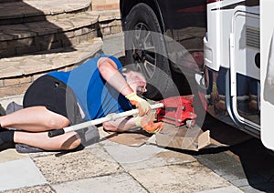 A male mechanic lying down as he places a red trolley jack under front of a motorhome recreational vehicle