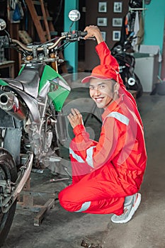 Male mechanic smiles while setting up the carburetor using the screwdriver next to the motorbike