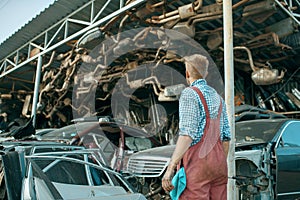 Male mechanic at the stack of cars on junkyard