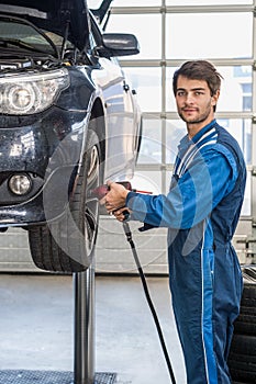 Male Mechanic Using Pneumatic Wrench To Fix Car Tire