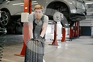 Male mechanic wearing gloves rolling tire for replacement at car service