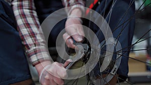 Male mechanic working in bicycle repair shop, mechanic repairing bike using special tool, wearing protective gloves