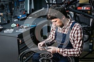 Male mechanic working in bicycle repair shop, mechanic repairing bike using special tool, wearing protective gloves. Young