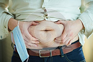 Male with medical mask checking body fat by grabbing stomach