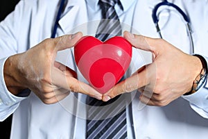 Male medicine doctor wearing hold in hands red toy heart