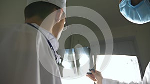 Male medics consult with each other while looking at x ray image. Medical workers in hospital examine x-ray prints. Two