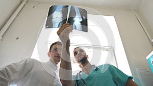 Male medics consult with each other while looking at x ray image. Two caucasian doctors view mri picture and discussing