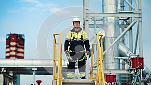 Male metalworker in safety helmet uniform contemplate construction refinery area from stairs