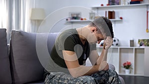 Male military praying, holding wooden cross in hand, remembering dead comrade