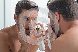 Male model applying cosmetic cream on face. Facial treatment. Beauty portrait of man applying face cream. Skin care