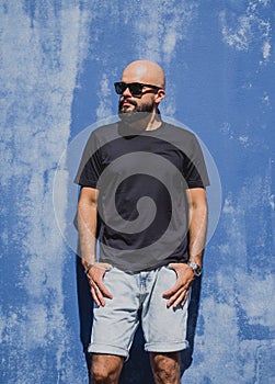 Male model with beard wearing black blank t-shirt on the background of an blue wall