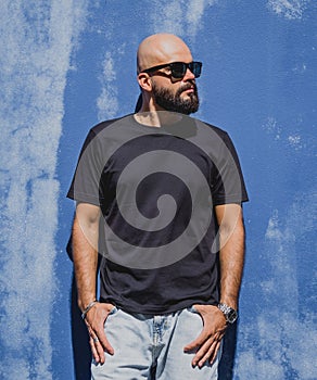 Male model with beard wearing black blank t-shirt on the background of an blue wall