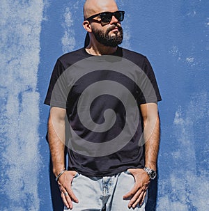 Male model with beard wearing black blank t-shirt on the background of an blue wall