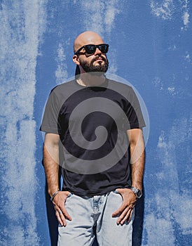 Male model with beard wearing black blank t-shirt on the background of an blue wall