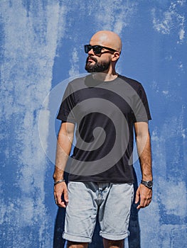 Male model with beard wearing black blank t-shirt on the background of an blue wall