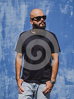 Male model with beard wearing black blank t-shirt on the background of an blue wall