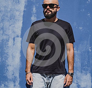Male model with beard wearing black blank t-shirt on the background of an blue wall