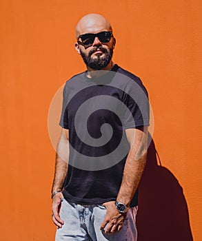 Male model with beard wearing black blank t-shirt on the background of an orange wall