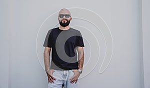 Male model with beard wearing black blank t-shirt on the background of an white wall