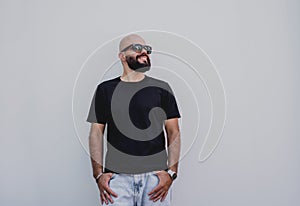 Male model with beard wearing black blank t-shirt on the background of an white wall